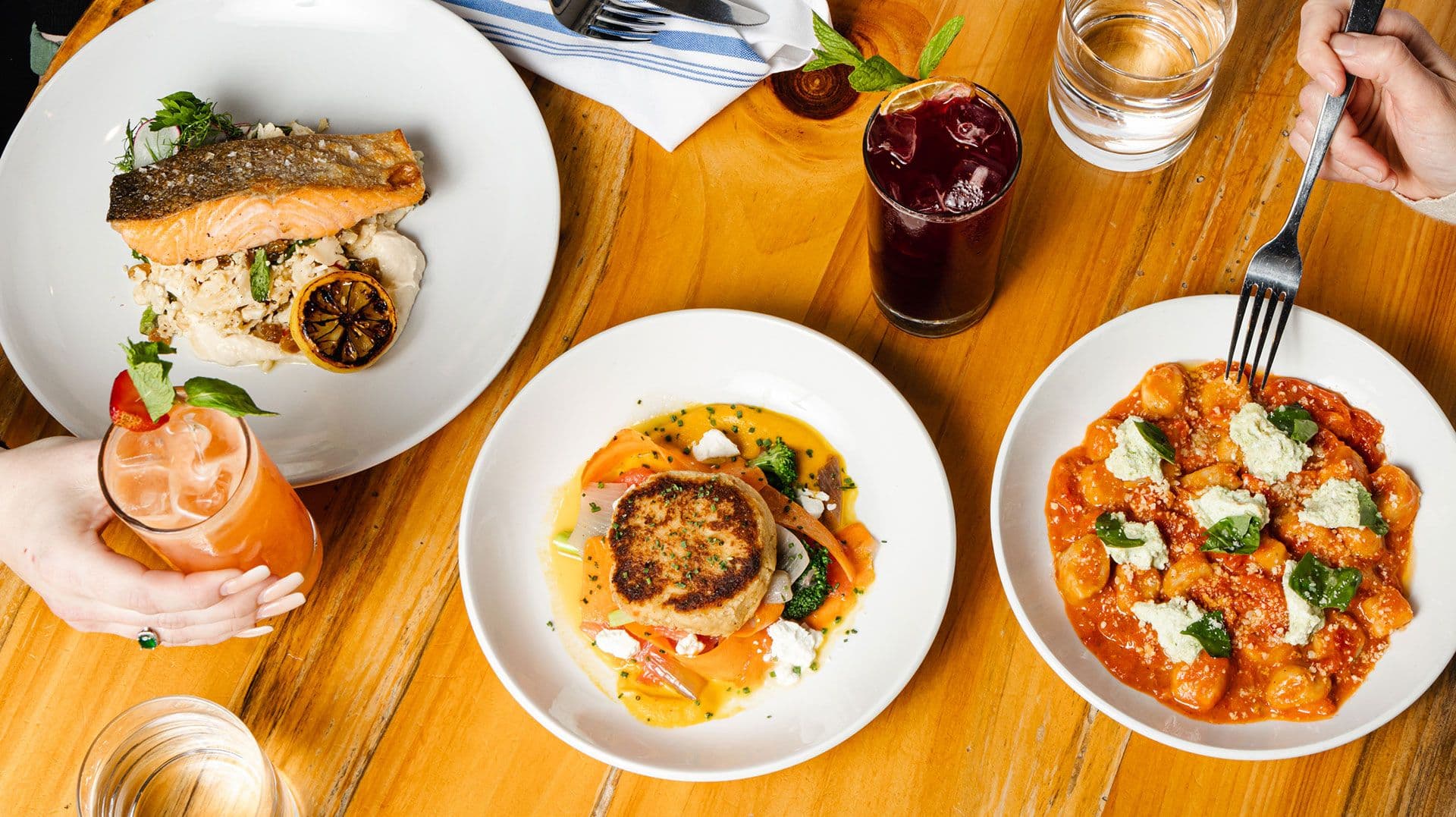 Overhead spread of scratch-made dishes and cocktails on a warm wood table at Crown Republic Gastropub in downtown Cincinnati